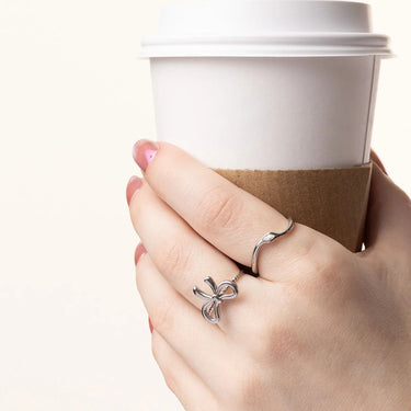 Hand holding a coffee cup with a silver bow ring on a white background