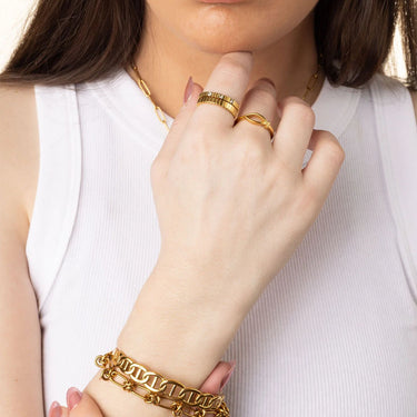 Close-up of a hand wearing gold jewelry including rings and a bracelet on a white background