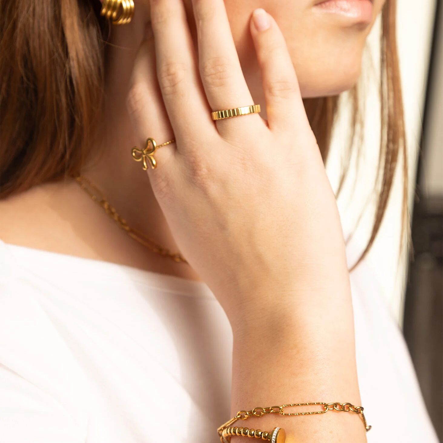 Close-up of a person wearing gold jewelry including earrings, rings, and bracelets.