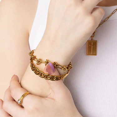 Close-up of a person's wrist wearing a gold bracelet with a cross pendant on a white background