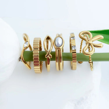 Gold rings with various designs on a green stick against a white background