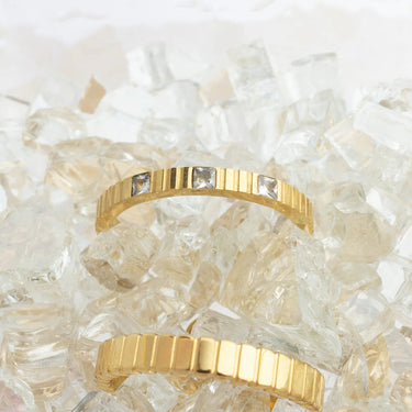 Two gold rings with diamond accents on a textured white surface