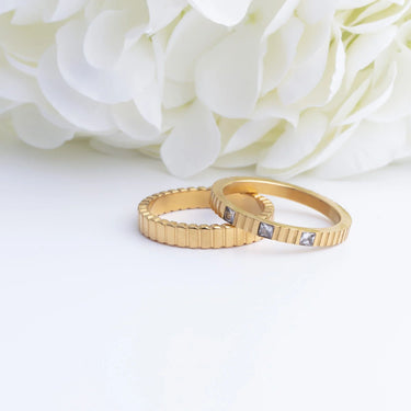 Two gold rings with diamond accents on a white background with white flowers.