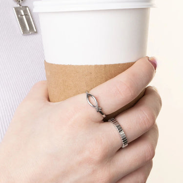 Hand wearing a silver ring holding a coffee cup with a cross pendant.