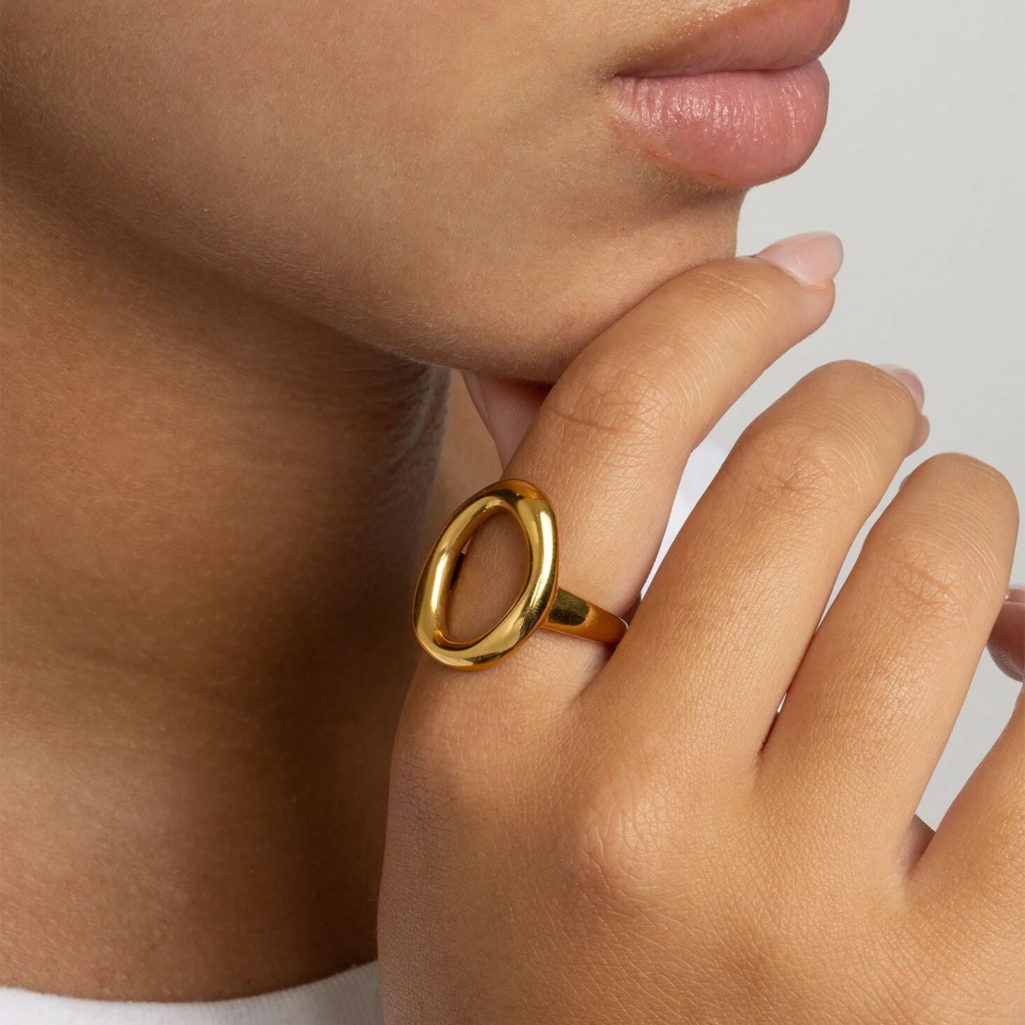 Close-up of a hand wearing a gold Oval Motif Ring  with a plain background