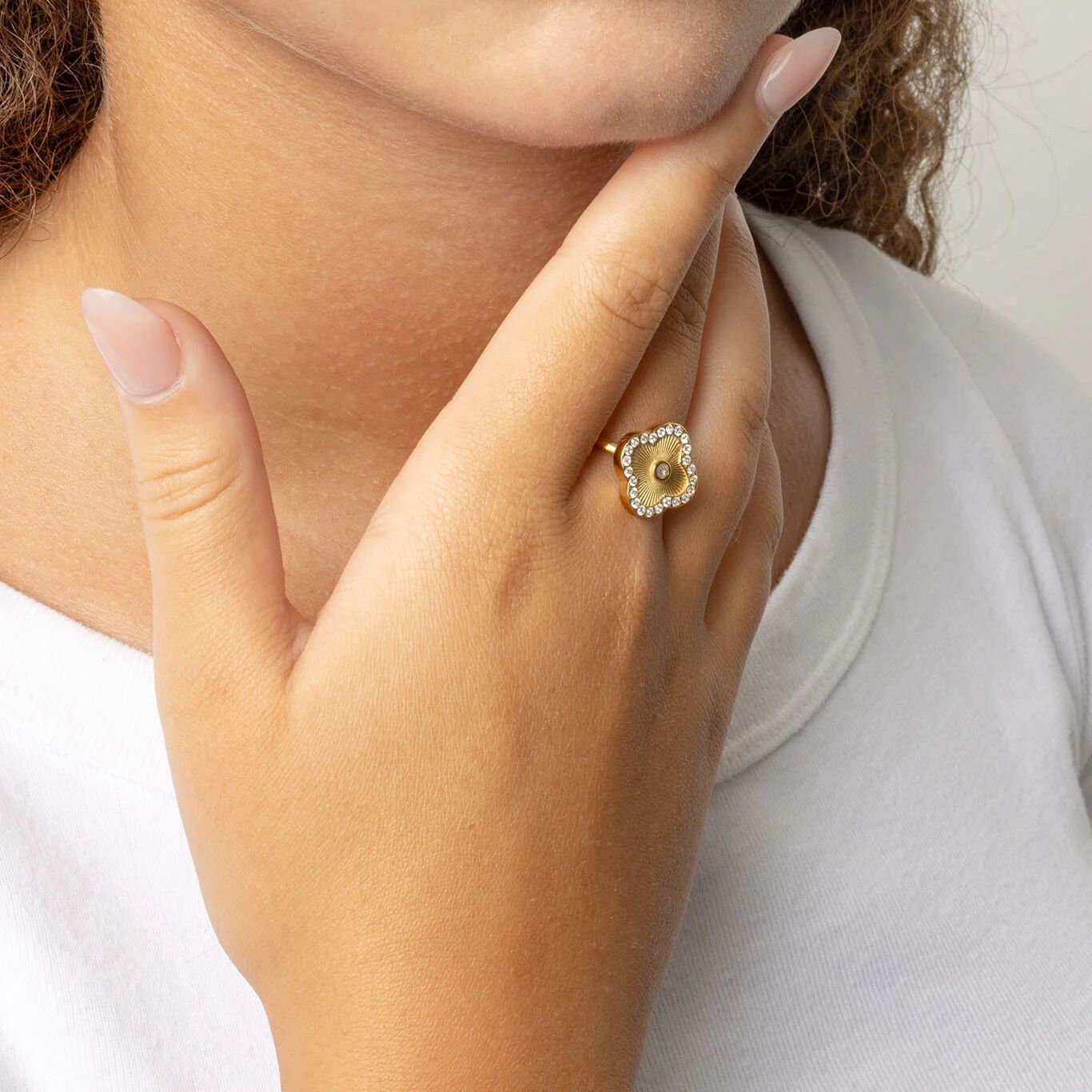 Close-up of a hand wearing a gold Floral Motif Ring with a clover design on a plain background