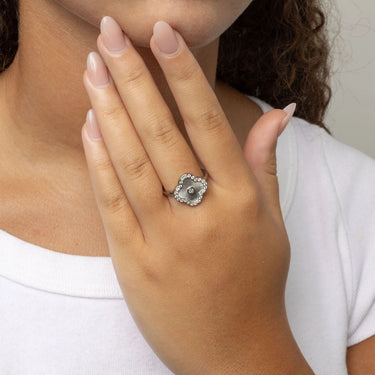 Close-up of a hand wearing a silver Floral Motif Ring with a central gemstone, against a neutral background.