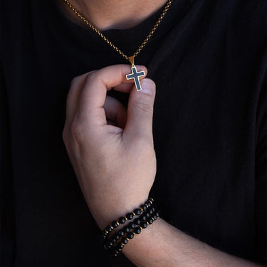 Hand holding a gold necklace with a cross pendant against a dark background