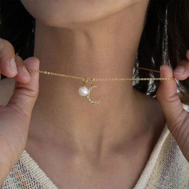 Gold anklet with a pearl and moon charm held by hands against a neutral background