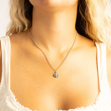Close-up of a necklace with a pendant on a person wearing a white top.