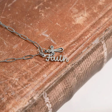 Silver necklace with 'Faith' pendant on a textured surface