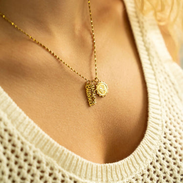 Gold necklace with heart-shaped pendants worn by a person in a beige sweater.