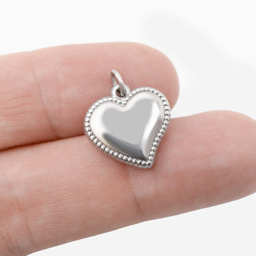 Silver heart-shaped pendant held between fingers on a white background