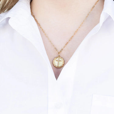 Gold necklace with a cross pendant worn by a person in a white shirt.