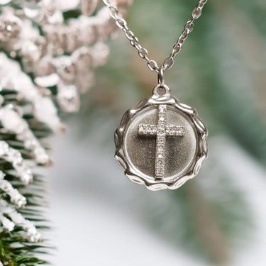 Silver necklace with a cross pendant against a blurred natural background
