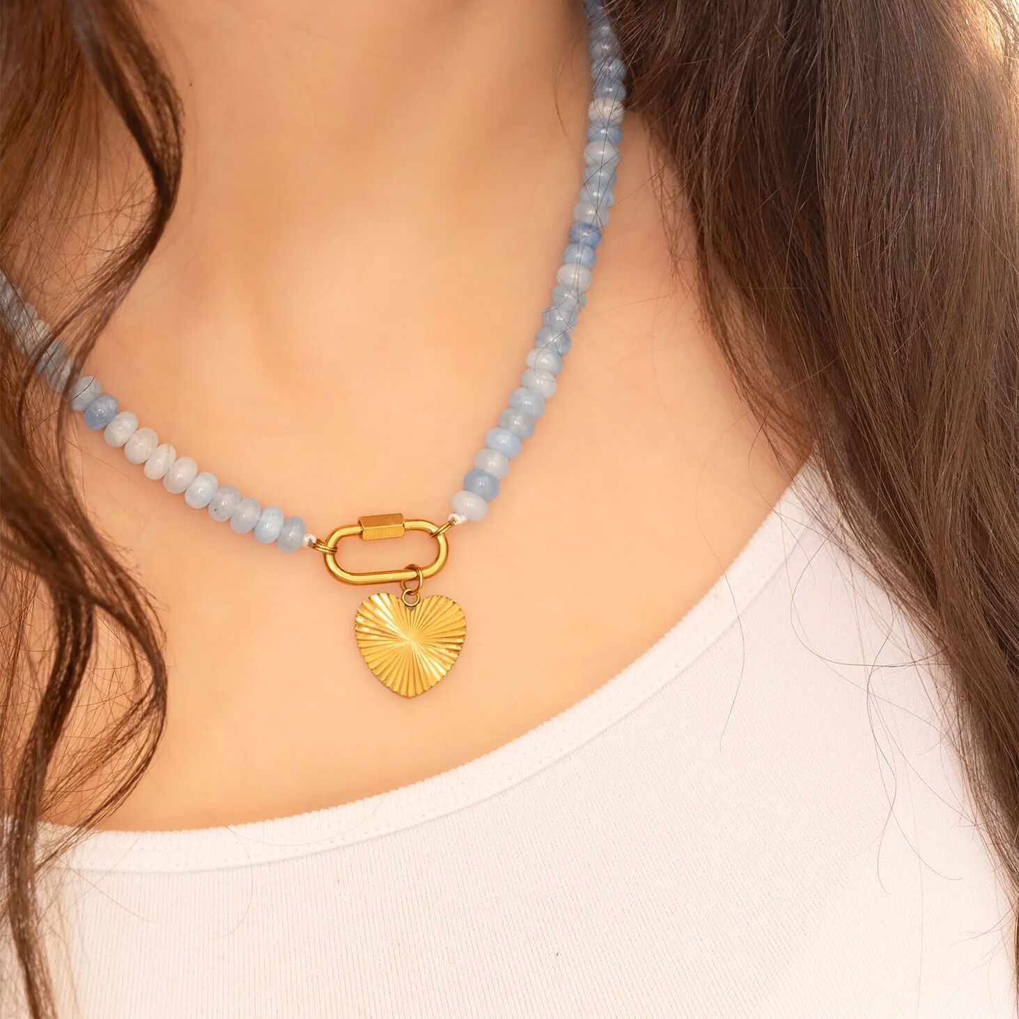 Necklace with blue beads and a gold heart pendant on a person wearing a white top.