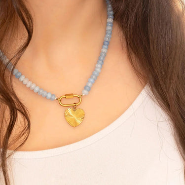 Necklace with blue beads and a gold heart pendant worn by a person.