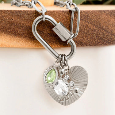 Silver necklace with heart-shaped pendant and green gemstone on a wooden surface