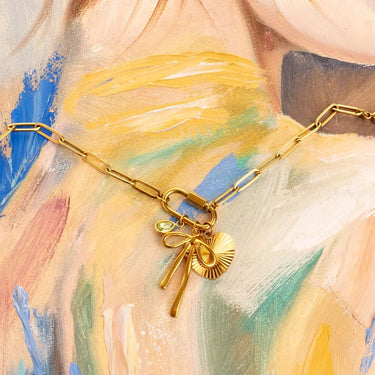 Gold necklace with a bow and round charm on a colorful abstract background
