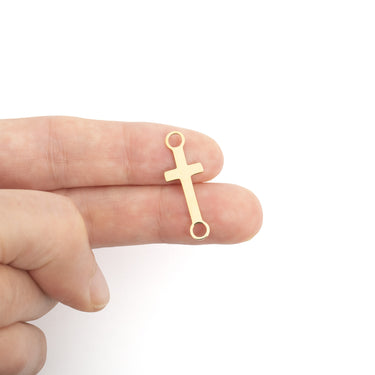 Gold cross-shaped pendant held between fingers on a white background