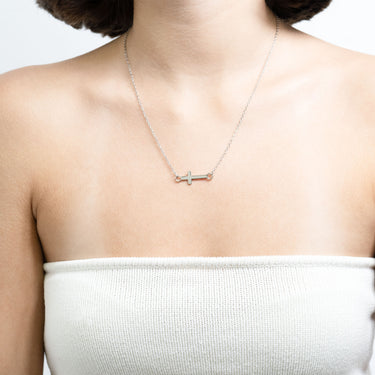 Necklace with a cross pendant on a person wearing a white top against a light background
