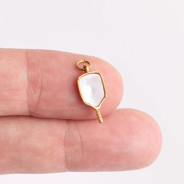Gold pendant with a white stone held between fingers on a light background