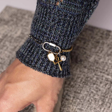 Close-up of a hand wearing a bracelet with charms on a textured surface