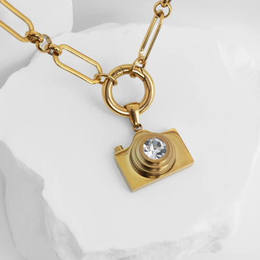 Gold camera-shaped pendant necklace on a white background