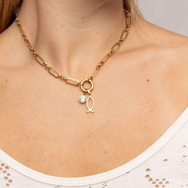 Gold chain necklace with a fish charm and clear gemstone on a person wearing a white top.