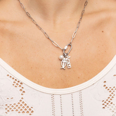 Silver necklace with a pendant and pearl on a person wearing a white top.