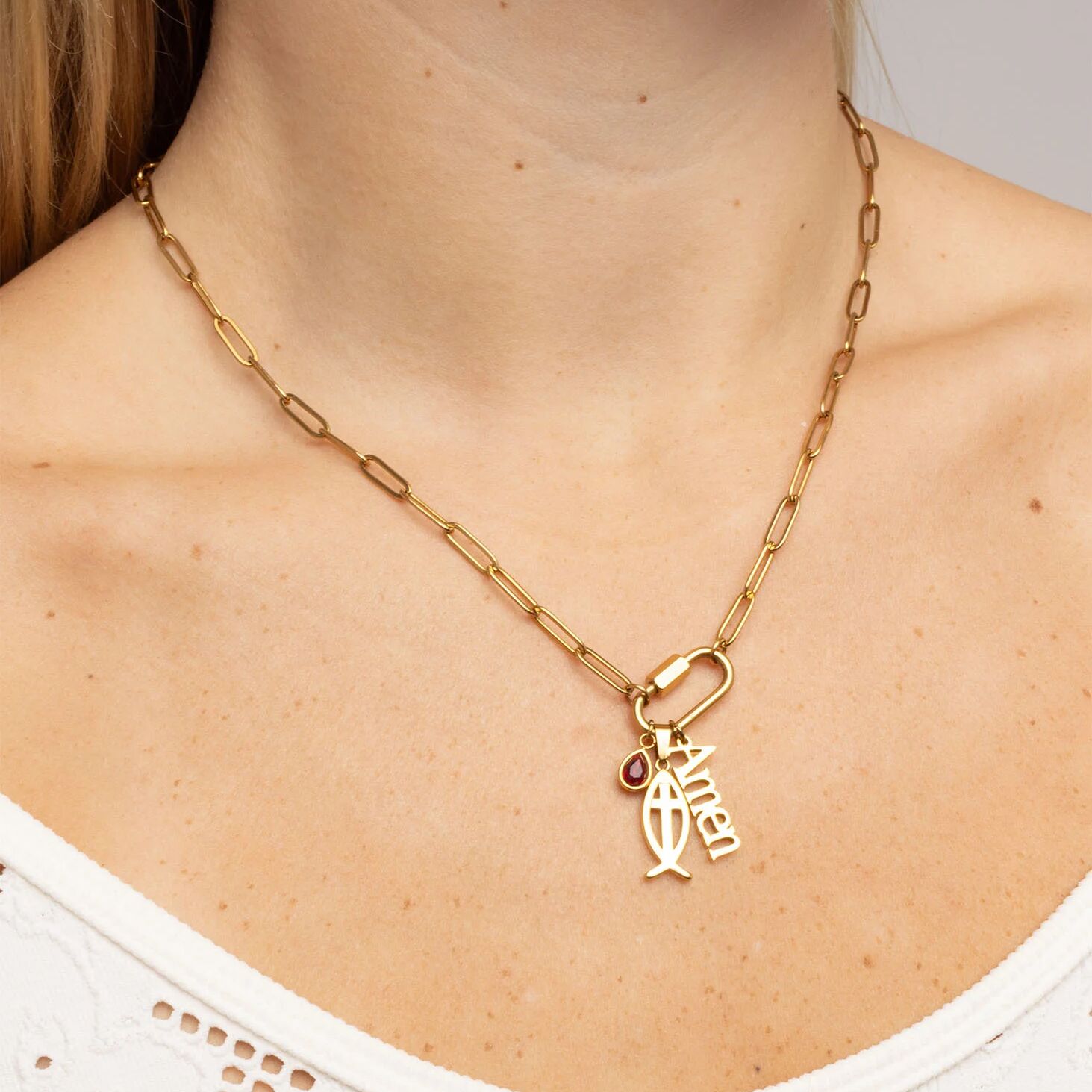 Gold necklace with a fish charm and red gemstone on a person wearing a white top.