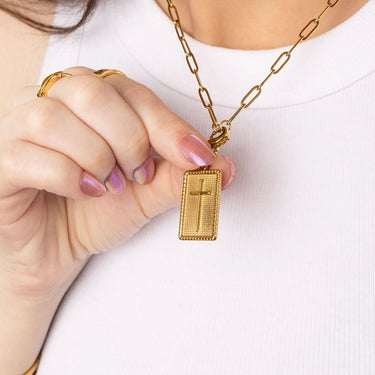 Gold necklace with a cross pendant held by a person against a white background