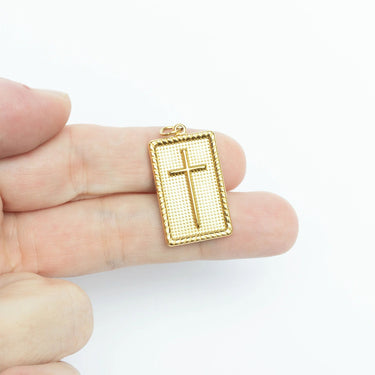 Gold cross pendant held between fingers on a white background