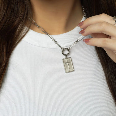 Silver necklace with a cross pendant worn by a person on a white background
