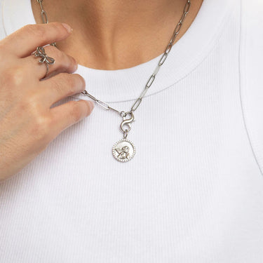 Person adjusting a silver necklace with a pendant on a white background