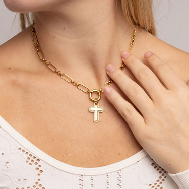 Gold necklace with a cross pendant worn by a person, with a hand touching the necklace.