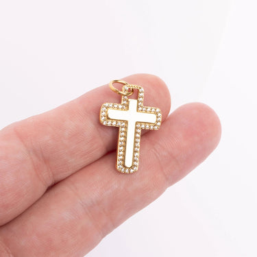 Gold cross pendant held in a hand for scale against a white background