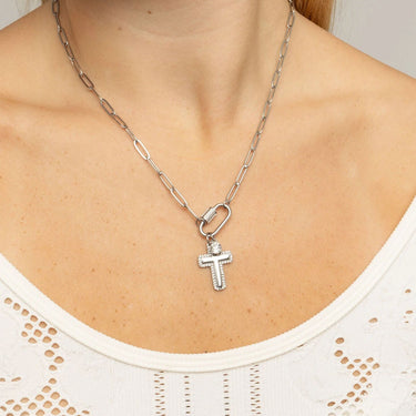 Silver necklace with a cross pendant worn by a person in a white top.