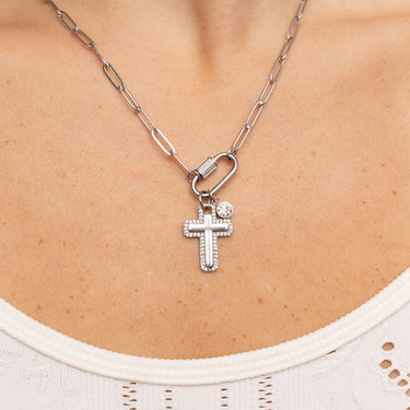 Silver necklace with a cross pendant on a person wearing a white top.