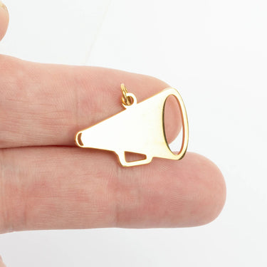 Gold megaphone pendant held between fingers on a white background