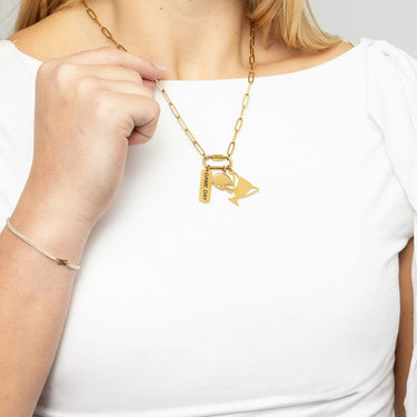 Gold necklace with charms held by a person wearing a white top