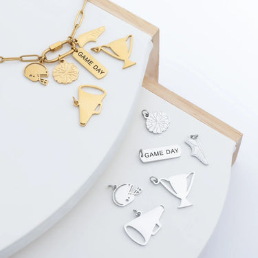 Gold and silver charm bracelets with various shapes and 'Game Day' text on a white surface.