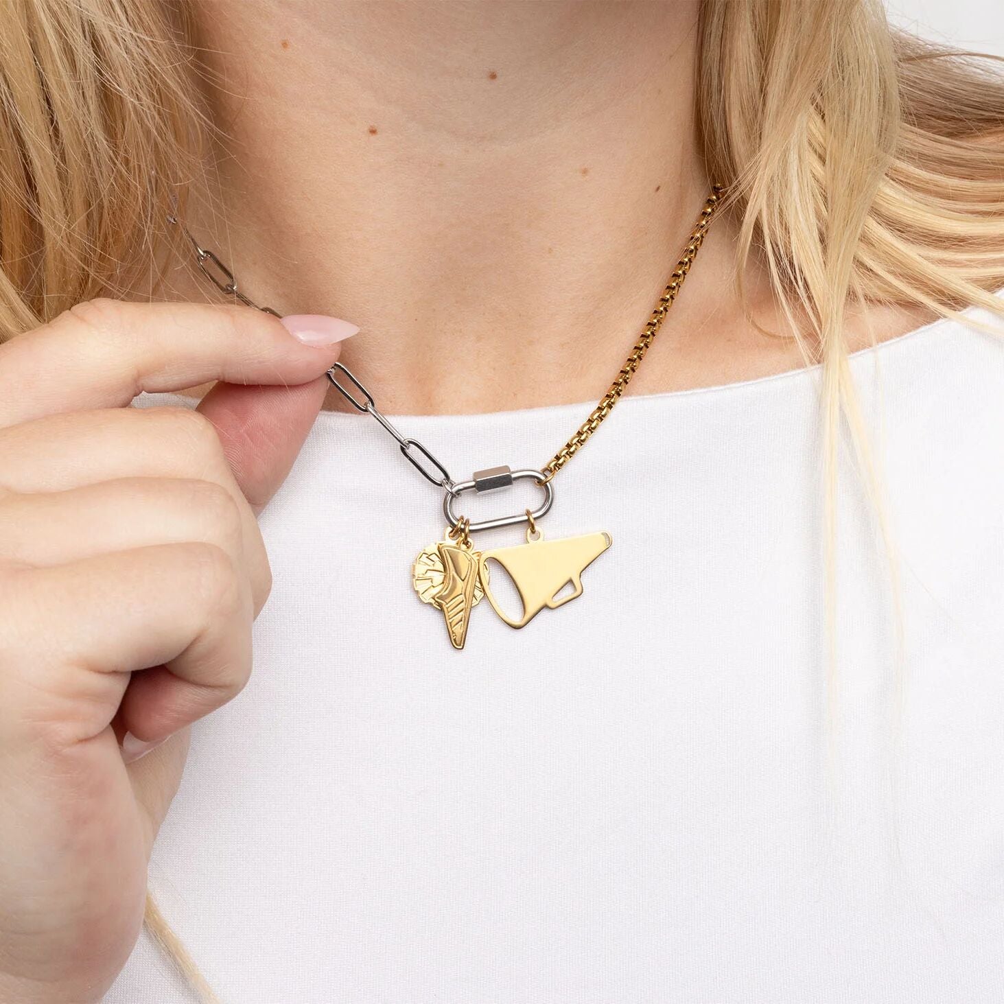 Gold necklace with a heart and megaphone charm being adjusted by a hand on a white background