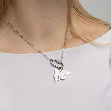 Silver necklace with a leaf pendant worn by a person on a plain background