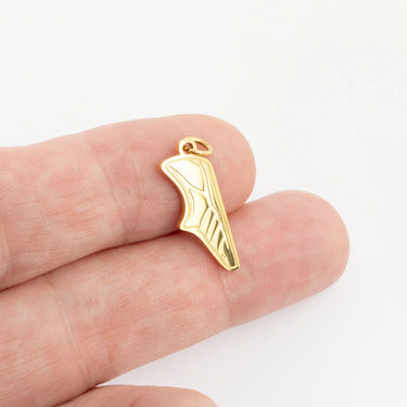Gold shoe charm held between fingers on a white background