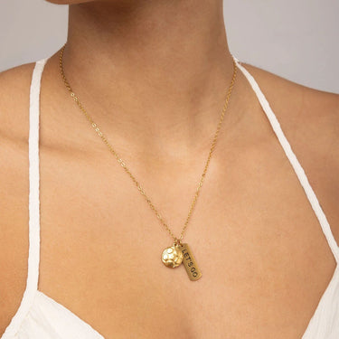 Gold necklace with a pendant on a person wearing a white top against a neutral background
