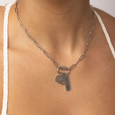 Silver chain necklace with a 'Let's Go' tag on a person wearing a white top.