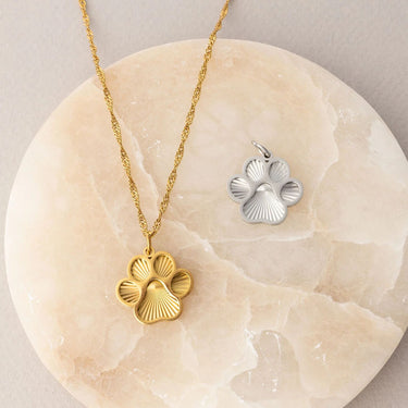 Gold and silver flower-shaped pendants on a beige stone surface