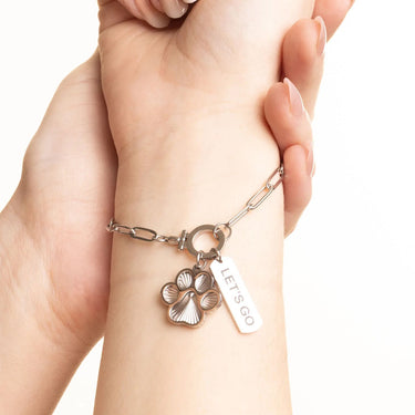 Bracelet with paw charm and 'LET'S GO' tag on a wrist against a white background