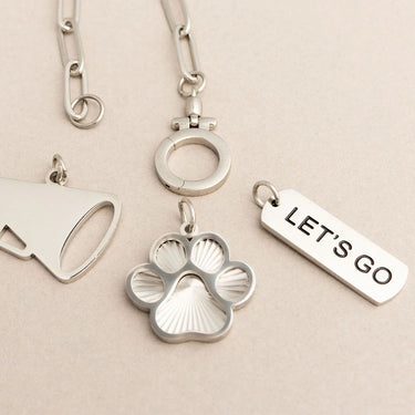 Silver keychain with paw print and 'LET'S GO' tag on a beige background